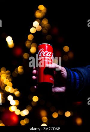 Belgrad, Serbien - 5. Januar 2023: Coca-Cola-Dose in der Hand mit Weihnachtslichtern und Dekorationen im Hintergrund bei Nacht in Belgrad, Serbien Stockfoto