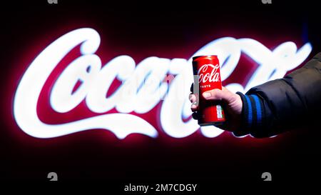 Belgrad, Serbien - 5. Januar 2023: Coca-Cola-Dose in der Hand mit Coca-Cola-Schild im Hintergrund bei Nacht in Belgrad, Serbien Stockfoto