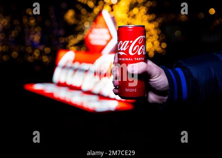 Belgrad, Serbien - 5. Januar 2023: Coca-Cola-Dose in der Hand mit Coca-Cola-Schild im Hintergrund bei Nacht in Belgrad, Serbien Stockfoto