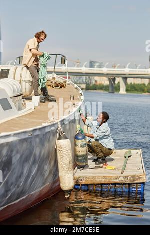 Vertikales Porträt von zwei Matrosen, Mann und Frau, die auf dem Boot in Docks arbeiten, beleuchtet von Sonnenlicht Stockfoto