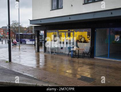Eine Frau, die vor einem Café in Newcastle-under-Lyme, Staffordshire, Großbritannien, einen Tisch abwischt Stockfoto
