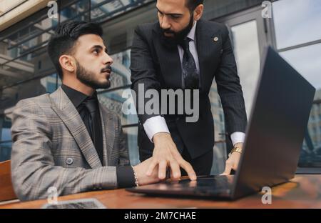 Geschäftstreffen im Freien. Eine Gruppe von Geschäftsleuten trifft sich im Freien. Zwei Männer benutzen einen Laptop. Arbeitspause. Team- und Business-Support Stockfoto