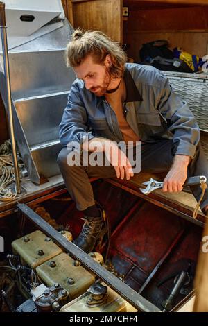 Vertikales Seitenbild eines bärtigen jungen Mannes, der eine Bootsmaschine repariert Stockfoto