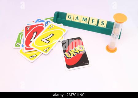 Das Konzept eines Spieleabends, in dem das Wort „Spiele“ in Scrabble-Fliesen auf einem Ziegelständer geschrieben wird. UNO-Karten werden auf einem Stapel mit einer Sanduhr verteilt. Stockfoto