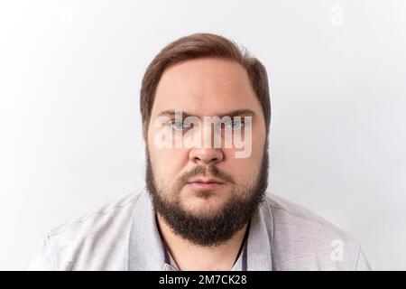 Ein ernster Mann mit einem Bart auf weißem Hintergrund in einem Hemd Stockfoto