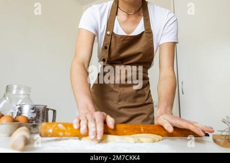 Eine Frau in einer Schürze bereitet den Teig für das Backen zu Hause vor. Ausrollen und Teig zum Backen vorbereiten. Stockfoto