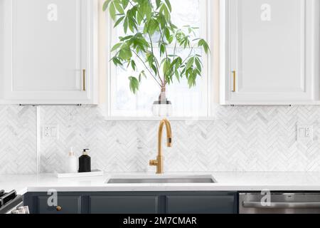 Waschbecken Detail in einer luxuriösen Küche mit Fischgrät backsplash Fliesen geschossen. Weißen Marmor Arbeitsplatte und Gold Wasserhahn. Stockfoto