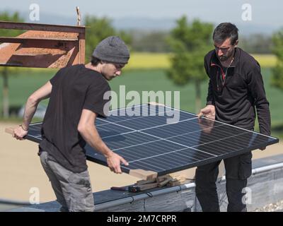 Männliche Teamingenieure, die eigenständige Solarpaneele installieren. Elektriker montieren blaues Solarmodul auf dem Dach des Unternehmens. Alternati Stockfoto