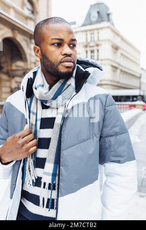 Junger afrikanischer Mann in legerer weißer und blauer Kleidung, gestreifter Pullover. Straßenporträt mit Schnee in der Wintersaison. Lifestyle, Stadtleben Konzept Stockfoto