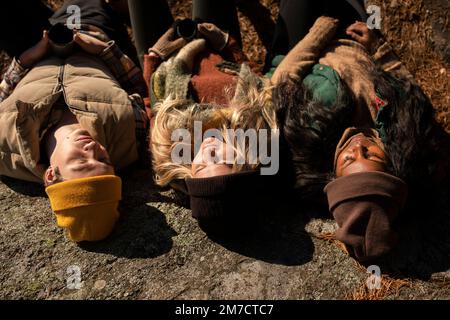 Männer und Frauen, die Strickmützen tragen und sich an sonnigen Tagen auf Felsen ausruhen Stockfoto