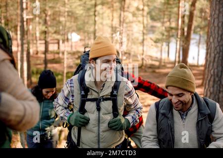 Glücklicher junger Mann, der mit einem männlichen Freund spricht, während er im Wald wandert Stockfoto