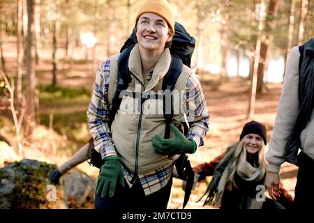 Glücklicher Mann, der wegsieht, während er mit Freunden im Wald wandert Stockfoto