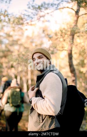 Seitenansicht eines lächelnden Mannes mit Rucksack, der im Wald steht Stockfoto