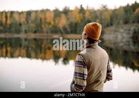 Rückansicht eines jungen Mannes mit Hand in der Tasche, der Zeit am See verbringt Stockfoto