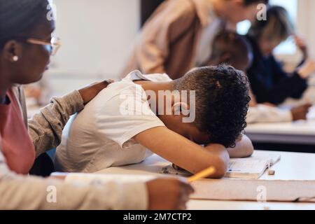 Studentin tröstet depressiven Teenager, der sich im Klassenzimmer auf dem Schreibtisch ruht Stockfoto