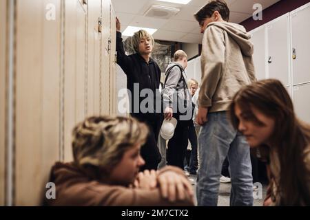 Ein Teenager, der Mädchen ansieht, die sich auf dem Schulflur unterhalten Stockfoto