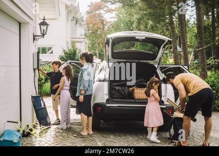 Laden und Verladen von Familiengepäck im Kofferraum eines Elektroautos außerhalb des Hauses Stockfoto