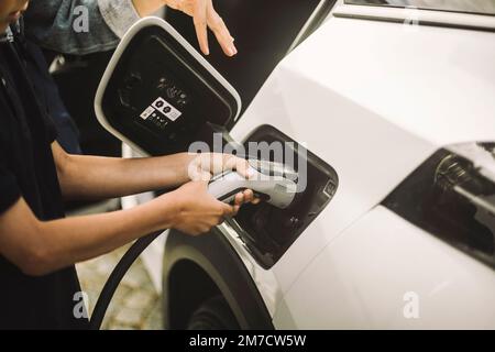 Hände eines Jungen, der beim Aufladen des Elektroautos Kabel einsteckt Stockfoto