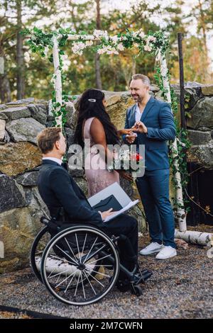 Fröhlicher Bräutigam und Braut, die bei der Hochzeitszeremonie den Ring tauschen Stockfoto