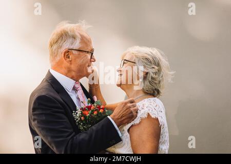 Seitenansicht eines lächelnden Senior-Paares, das sich anschaut und an der Wand steht Stockfoto