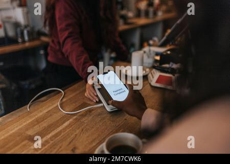 Hand eines weiblichen Kunden, der kontaktlose Zahlungen über ein Smartphone bei der Kasse im Café tätigt Stockfoto