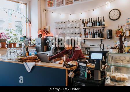 Lächelnde junge Besitzerin, die beim Auschecken im Café über einen Laptop mit einem Kollegen sprach Stockfoto