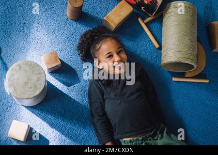 Porträt eines lächelnden Mädchens mit auf dem Teppich liegendem Spielzeug in der Kinderbetreuung Stockfoto