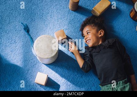 Direkt über dem Bild eines lächelnden Mädchens, das auf einen hölzernen Spielzeugblock im Kindergarten schaut Stockfoto