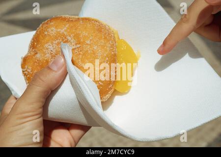Handgehaltenes Bola de Berlim oder Berlim Ball, ein portugiesisches Gebäck aus gebratenem Donut gefüllt mit süßer Eiercreme und in knusprigem Zucker gerollt Stockfoto