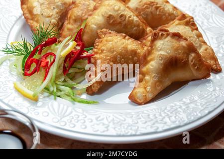 Asiatische gebratene Knödel mit Soja und süßer Sauce auf weißem Gericht. Gebratene Teigtaschen Gyoza mit Sojasauce und Essstäbchen, selektiver Fokus. Stockfoto