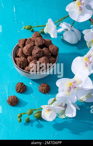 Handgemachte rustikale Schokoladentrüffel mit weißen Orchideenblumen auf türkisfarbenem Hintergrund Stockfoto