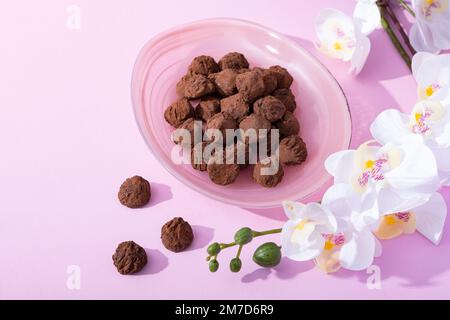 Handgemachte rustikale Schokoladentrüffel mit weißen Orchideenblumen auf pinkfarbenem Hintergrund Stockfoto