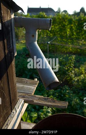 Ein Kunststoff-Regenrohr wird verwendet, um Wasser aus einem Schuppendach auf einem Pflaster zu sammeln. Stockfoto