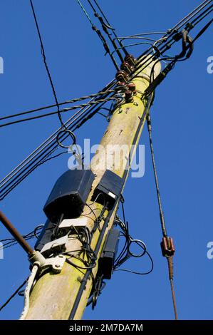 Ein Telegrafenmast steht vor einem tiefen blauen Himmel, der am Holzpfosten befestigt ist, und besteht aus vielen verschiedenen Drähten, einschließlich Netzleitungen, Telefonleitungen usw. Stockfoto