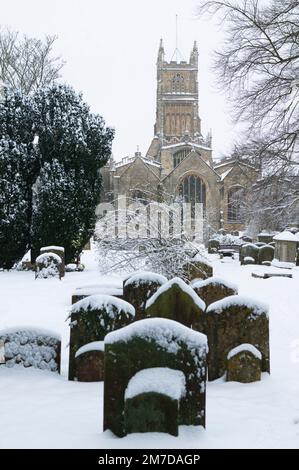 Das Gelände der Kirche St. John the Baptist in Cirencester, Großbritannien, mit Friedhof im tiefen Schnee des Winters. Versteckt im Schnee stehen die Grabsteine in dieser friedlichen, ruhigen Szene, die typisch für den traditionellen britischen Winter ist. Stockfoto