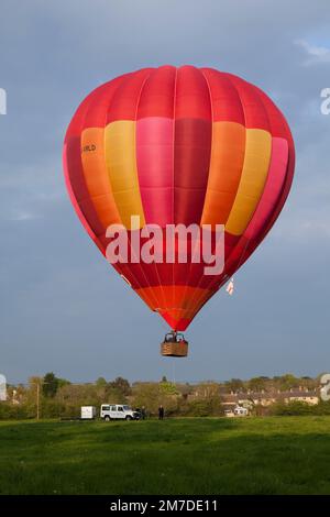 Eine helle rote Heißluft-Ballon abhebt von einem Feld in den Cotswolds, die Passagiere auf einem Rundflug. Stockfoto