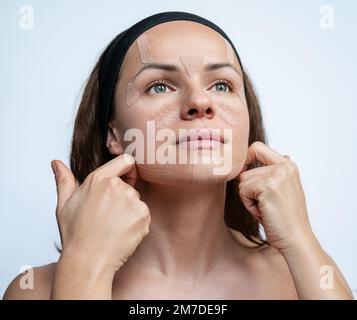 Attraktive Frau, die ein kinesiologisches Klebeband auf ihr Gesicht aufklebt Hautpflege. Stockfoto