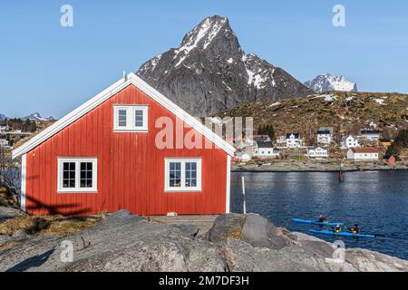 Menschen, die Kajakfahren entlang des Fjords, umgeben von traditionellen Rorbu-Häusern, reine, Nordland, Lofoten-Inseln, Norwegen Stockfoto