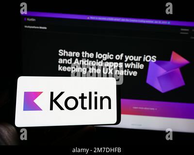 Person mit Mobiltelefon mit Logo der Programmiersprache Kotlin auf dem Bildschirm vor der Webseite. Konzentrieren Sie sich auf das Display des Telefons. Stockfoto