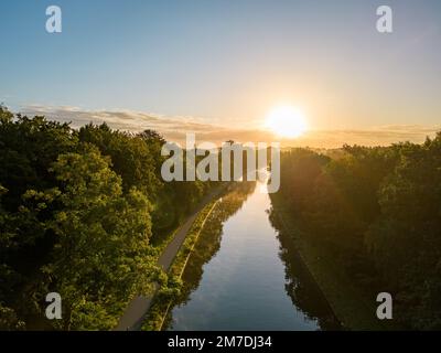 Von einer Drohne aus der Vogelperspektive sehen Sie den Sonnenaufgang oder -Untergang hinter dem Fluss und füllen die Bäume mit warmem Abendlicht, der Nebel steigt in den goldenen Lichtstrahlen auf. Wolken und Wolken werden im Wasser reflektiert. . Hochwertiges Foto Stockfoto