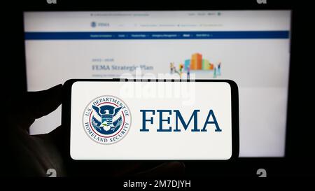 Person, die ein Mobiltelefon mit dem Siegel der Federal Emergency Management Agency (FEMA) auf dem Bildschirm vor der Webseite hält. Konzentrieren Sie sich auf das Display des Telefons. Stockfoto