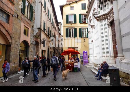 Alltag, Menschen, Straßenverkäufer, Touristen, Einheimische auf der Via Fillungo vor der entsezten Kirche des Heiligen Christopher, Lucca, Toskana, Italien. Stockfoto