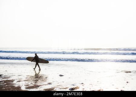 Surfer mit Surfbrett am Strand von Großbritannien Stockfoto