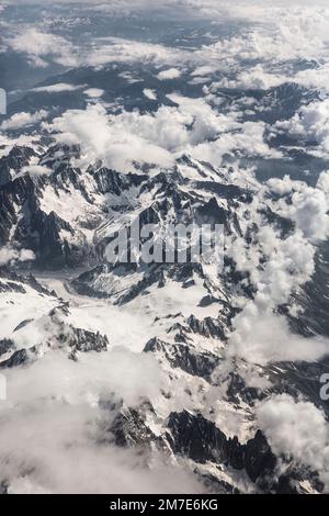 Die dünne, weiche Wolke bedeckt das Berggebiet der Alpen aus der Sicht eines Flugzeugfensters, das über uns fliegt. Stockfoto