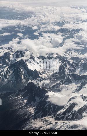 Die dünne, weiche Wolke bedeckt das Berggebiet der Alpen aus der Sicht eines Flugzeugfensters, das über uns fliegt. Stockfoto