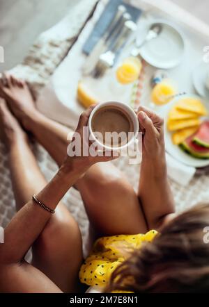 Detailansicht einer Frau, die im Hotelbett frühstückt und ihre Tasse Kaffee hält. Konzept von Urlaub und Entspannung im Strandhotel. Stockfoto