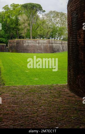 Blick über die Grünflächen, durch die dicke Renaissance-Mauer, in Richtung eines anderen Abschnitts der historischen Stadtmauer von Lucca, der Toskana, Italien. Stockfoto