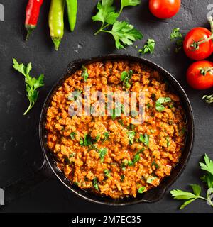 Keema Curry in gusseiserner Pfanne auf schwarzem Steinhintergrund. Indisches und pakistanisches Gericht. Draufsicht, flach liegend Stockfoto