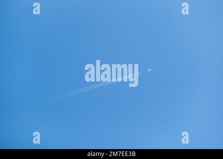 Ein Düsenflugzeug fliegt über den Kopf durch die Lichtwolke. Verschwindet hinter der weißen Schicht, die vor einem blauen Himmel steht. Stockfoto