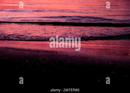 Kleine Wellen Rollen bei Sonnenuntergang zu einem Sandstrand mit verwischten Wellen und rollendem Wasser. Stockfoto